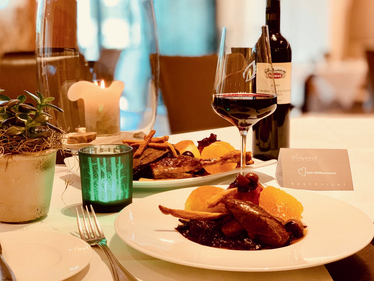Gedeckter Tisch mit Rotwein und Hauptgericht im Restaurant des Landidyll Hotels Birkenhof